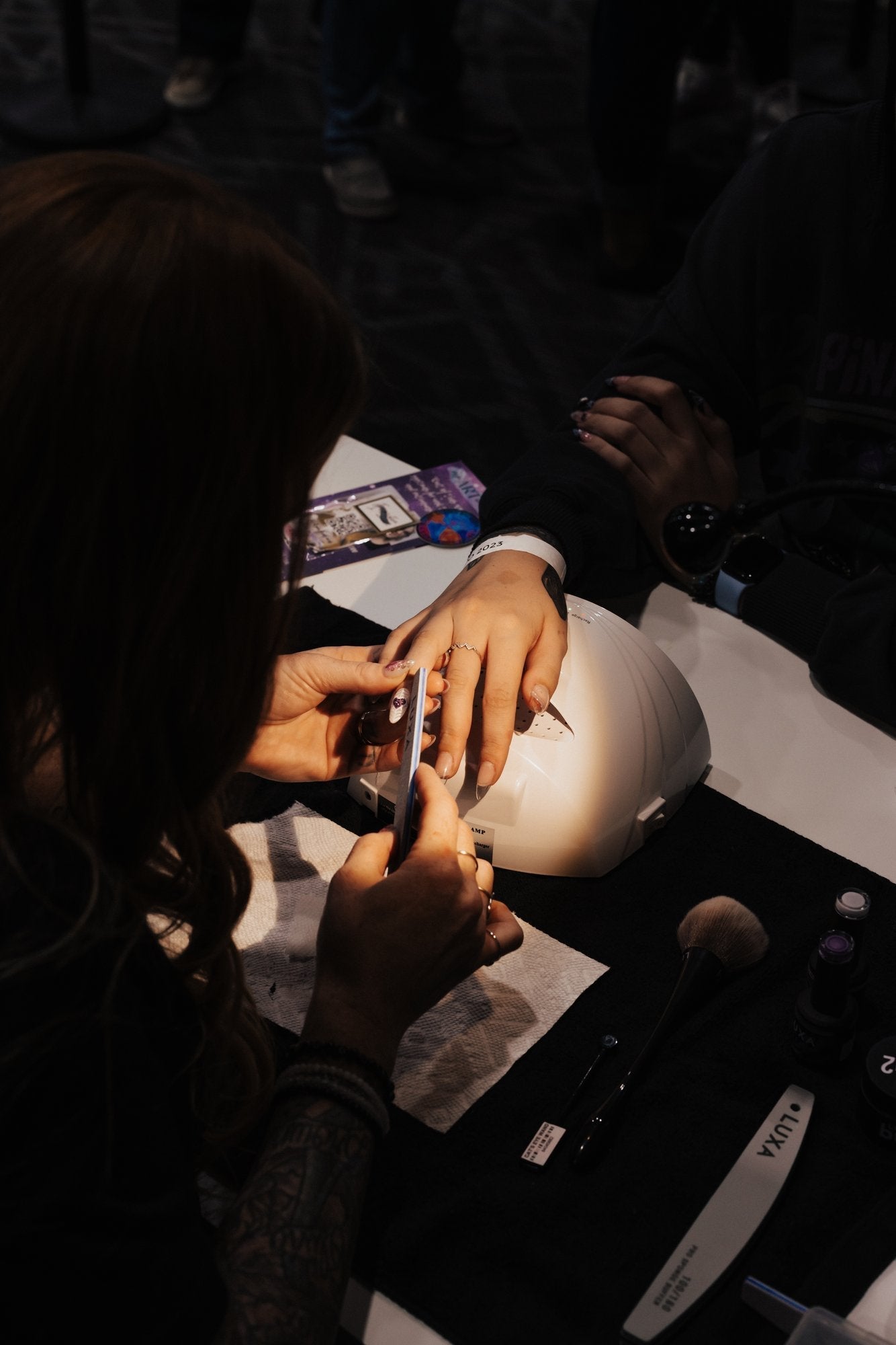 Manicurist filing a client’s nails over a UV lamp at a manicure station
