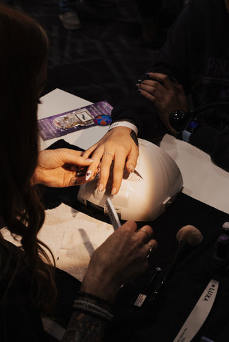 Nail technician filing a client’s nails at a salon workstation with an LED nail lamp