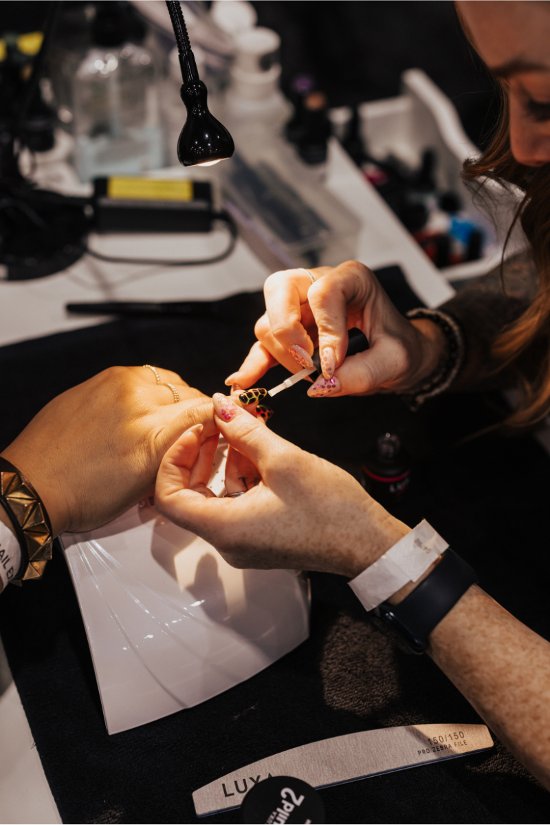 Nail technician applying detailed nail art to a client’s hand at a salon workstation