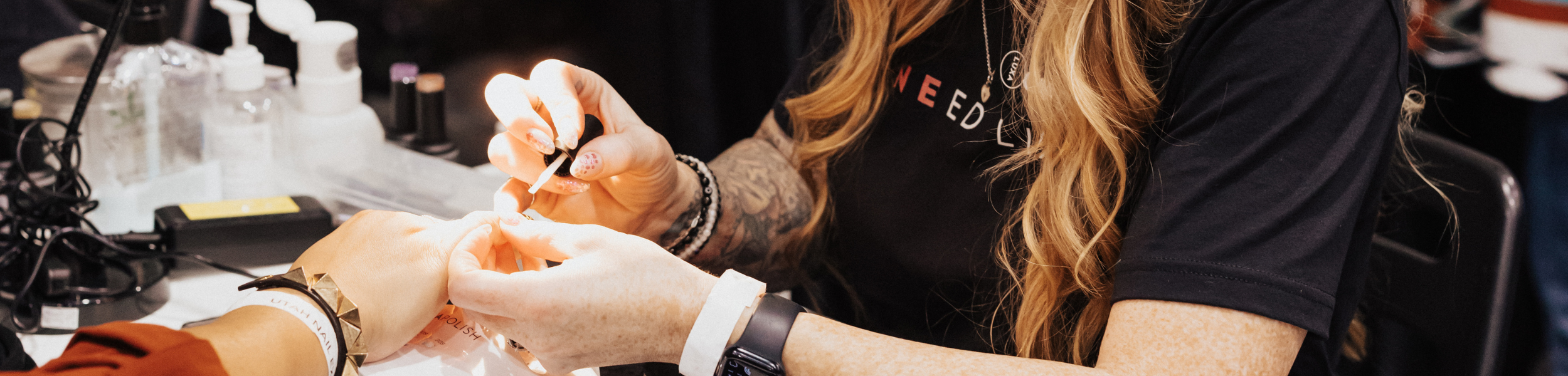 Nail technician painting a client’s nails at a salon station with manicure tools on the table