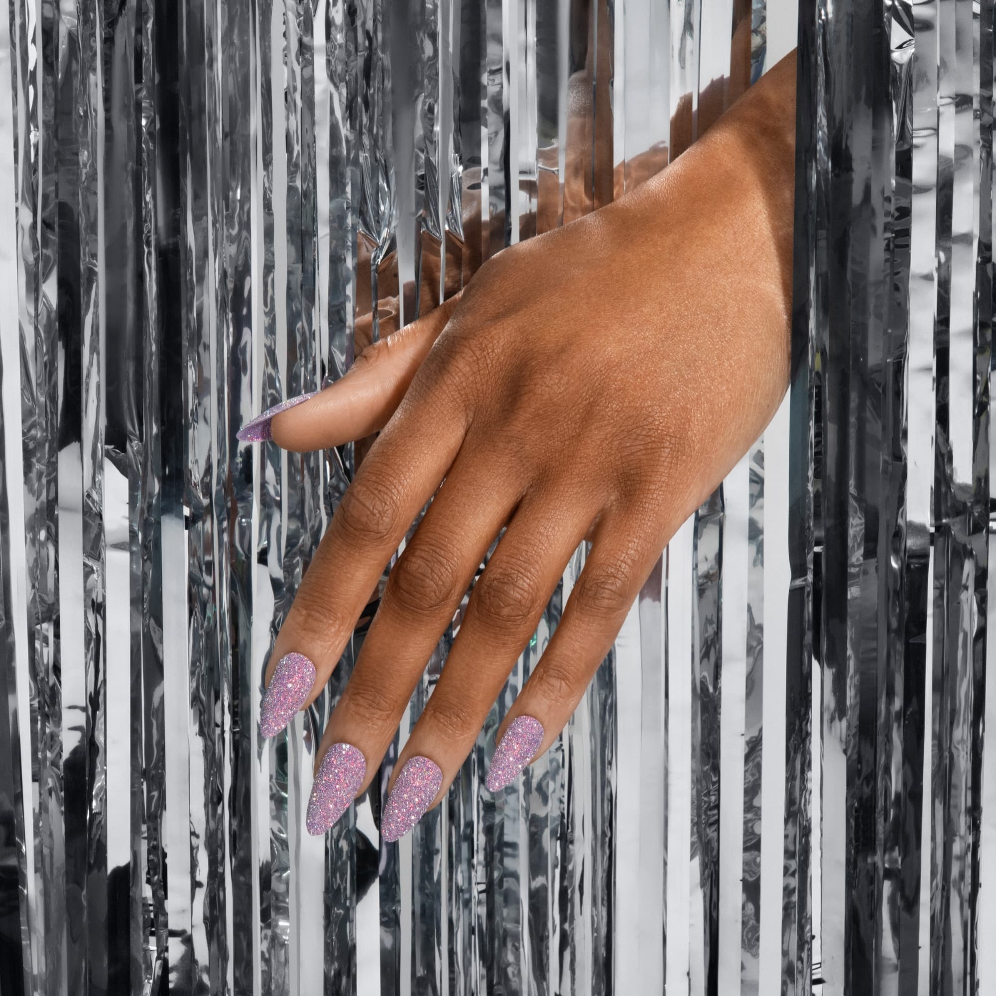 Hand displaying long pink glitter nails against silver tinsel