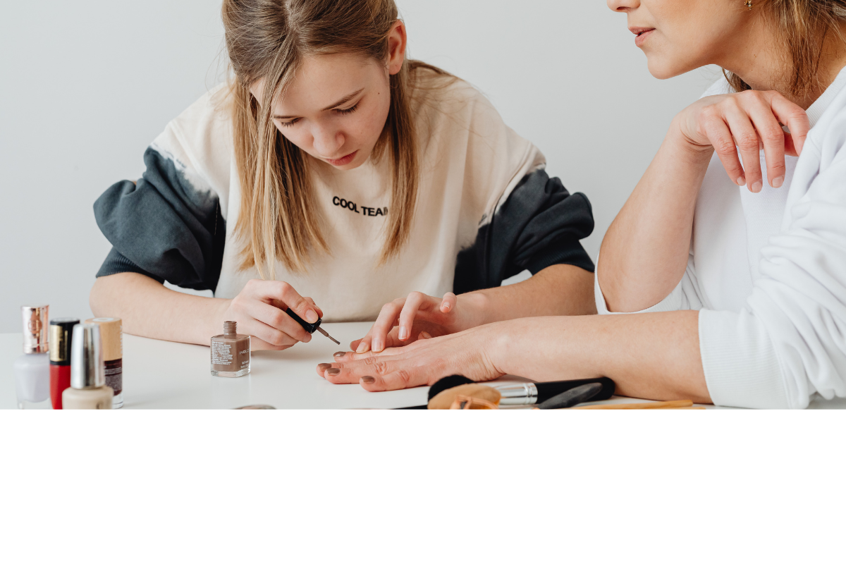Woman painting a client’s nails at a table with nail polish bottles and brushes nearby