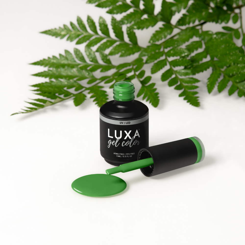 Three-quarter view of LUXA Gel Fresh Out of Ferns 15mL bottle and brush showing spilled fern-green polish with fern leaves backdrop