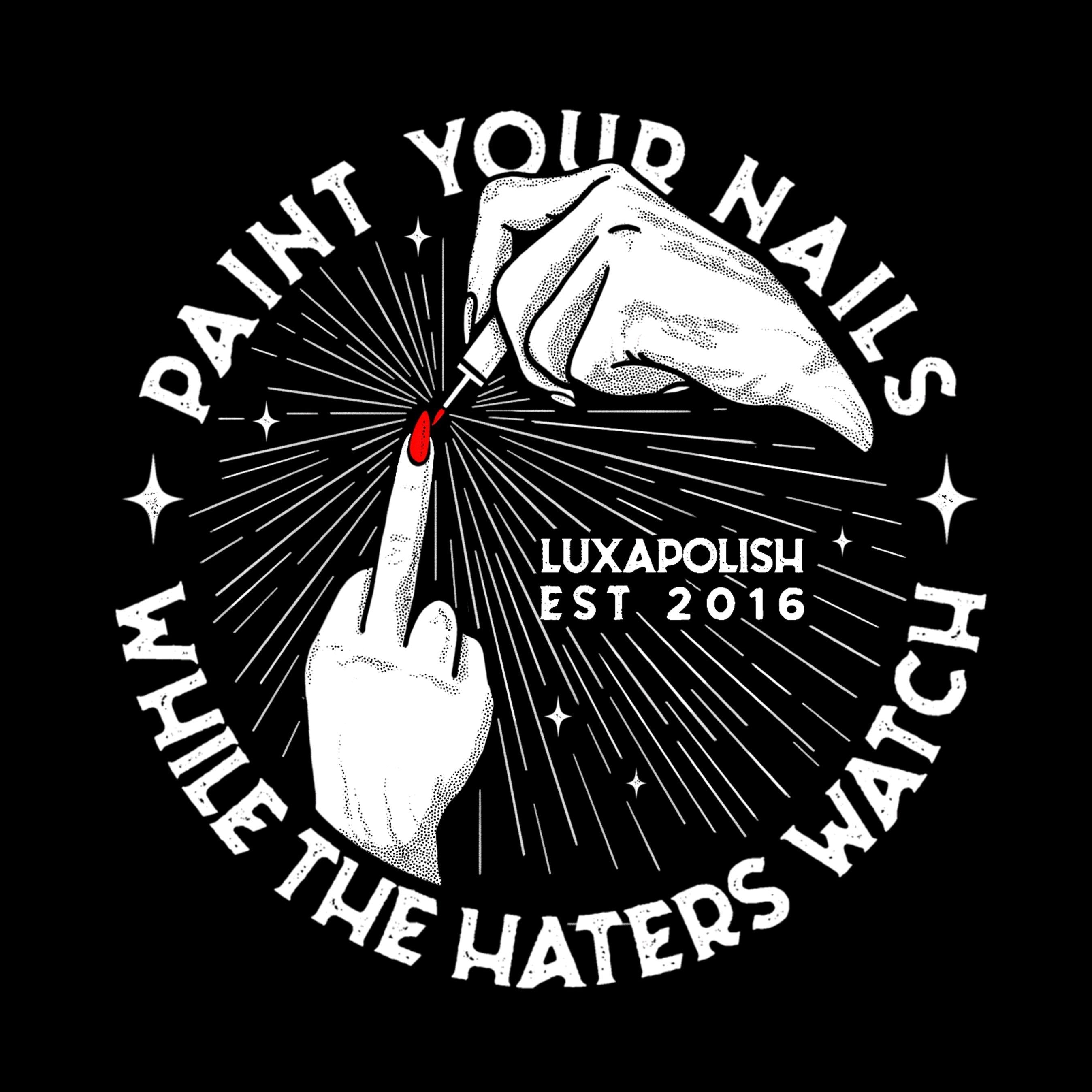 Close-up of black tee back graphic showing ‘Paint Your Nails’ arched text, a hand painting a red nail and LUXAPOLISH logo