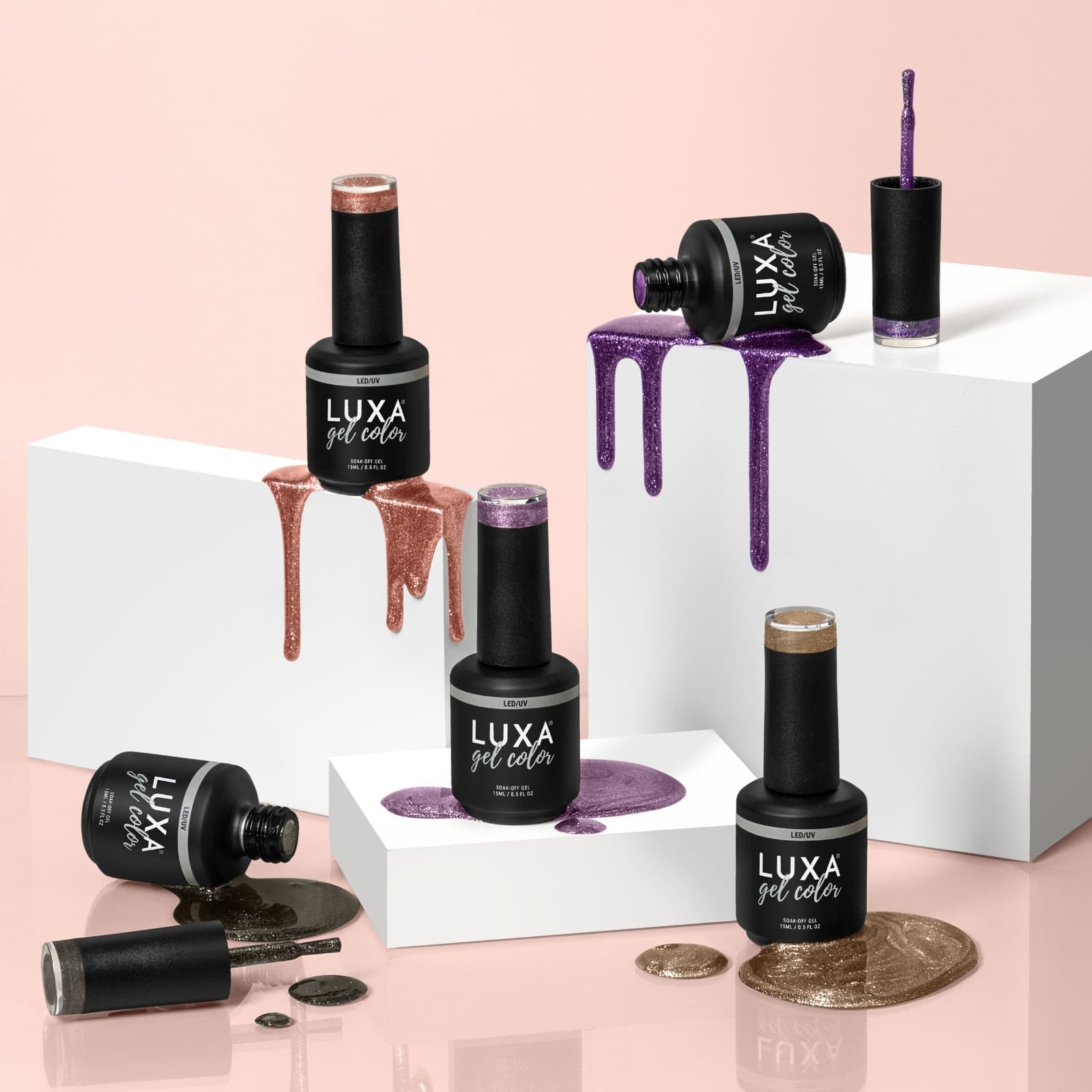 Front view of LUXA gel color bottles with glittery purple and rose gold polish spilling over white blocks on pink background
