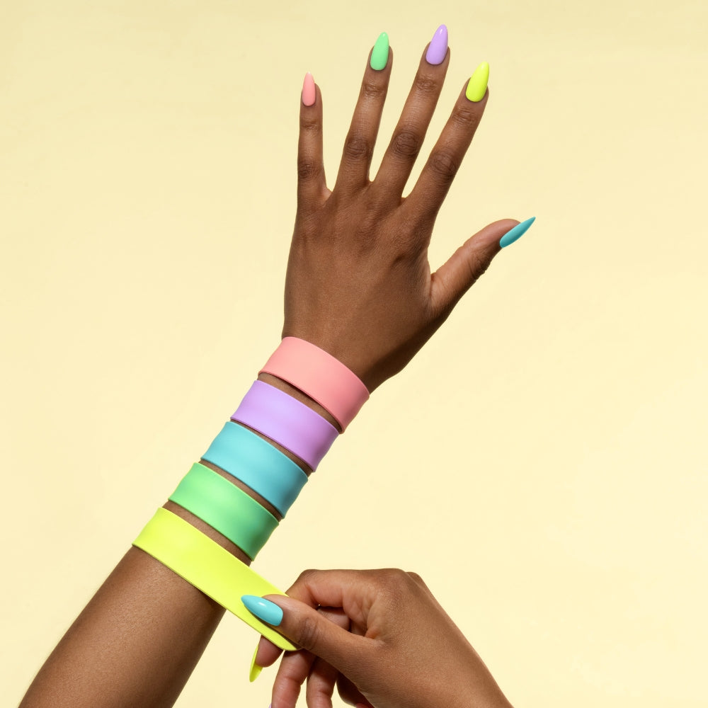 Hand with long pastel gel nails adjusting neon slap bracelets against a pale yellow background
