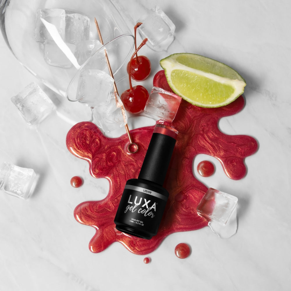 Top down view of LUXA gel color bottle on a spilled shimmery red polish swatch with cherries, lime and ice