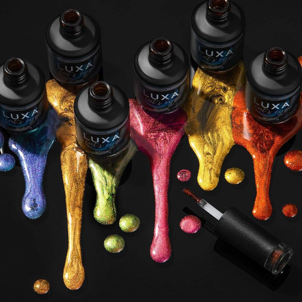 Top-down view of Luxa cat’s eye gel polish bottles spilling multicolored metallic shimmer on a black surface with an applicator brush